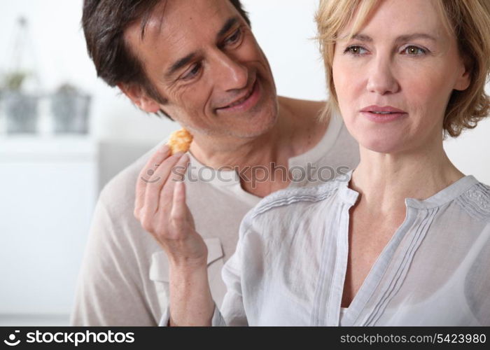 Woman in kitchen holding food in hand man looking at her