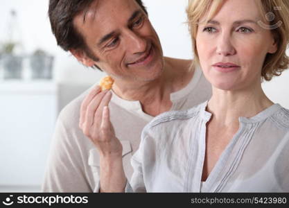 Woman in kitchen holding food in hand man looking at her