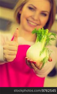 Woman in kitchen holding green fresh raw fennel bulb vegetable. Housewife cooking meal. Healthy eating, vegetarian food, dieting concept.. Woman holding fennel bulb