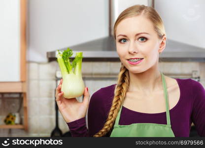 Woman in kitchen holding green fresh raw fennel bulb vegetable. Young housewife cooking. Healthy eating, vegetarian food, dieting and people concept.. Woman in kitchen holds raw fennel bulb vegetable