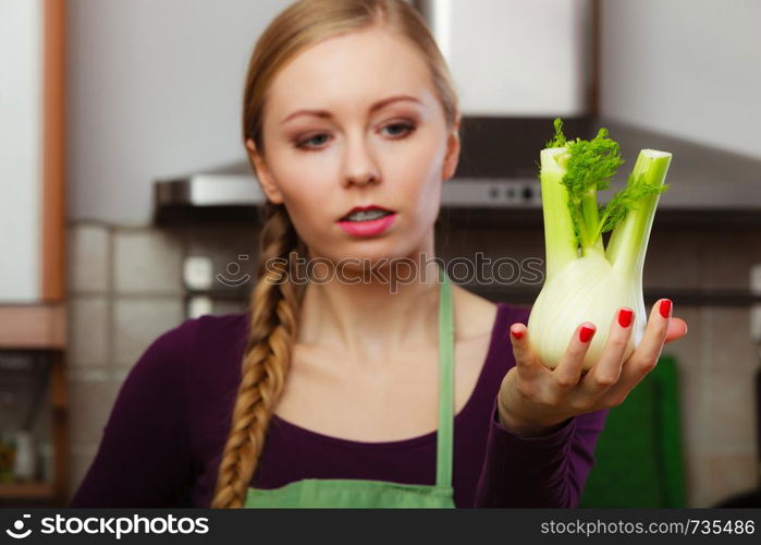 Woman in kitchen holding green fresh raw fennel bulb vegetable. Young housewife cooking. Healthy eating, vegetarian food, dieting and people concept.. Woman in kitchen holds raw fennel bulb vegetable