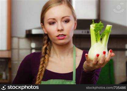 Woman in kitchen holding green fresh raw fennel bulb vegetable. Young housewife cooking. Healthy eating, vegetarian food, dieting and people concept.. Woman in kitchen holds raw fennel bulb vegetable