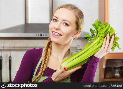 Woman in kitchen holding green fresh stemmed celery. Young housewife cooking. Healthy eating, vegetarian food, dieting and people concept.. Woman in kitchen holds green celery
