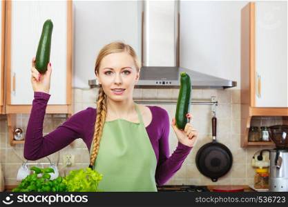 Woman in kitchen holding green fresh zucchini vegetable. Young housewife cooking. Healthy eating, vegetarian food, dieting and people concept.. Woman in kitchen holds zucchini vegetable