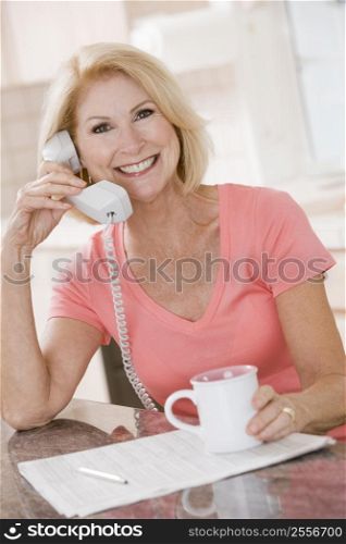 Woman in kitchen using telephone and smiling