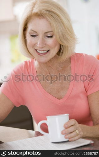 Woman in kitchen with coffee and newspaper smiling