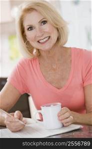 Woman in kitchen with coffee and newspaper smiling