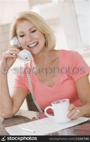 Woman in kitchen with coffee using telephone smiling