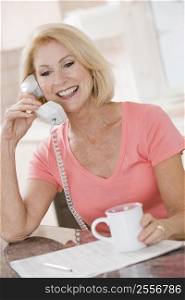 Woman in kitchen with coffee using telephone smiling