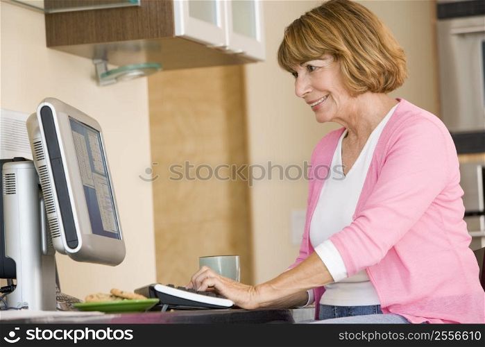 Woman in kitchen with computer and coffee smiling