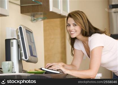 Woman in kitchen with computer smiling