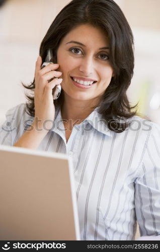 Woman in kitchen with laptop and cellular phone smiling