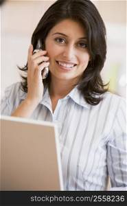 Woman in kitchen with laptop and cellular phone smiling