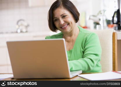 Woman in kitchen with laptop smiling