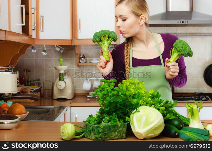 Woman in kitchen with many green leafy vegetables, fresh produce on counter. Young housewife holding broccoli in hand. Healthy eating, cooking, vegetarian food, dieting and people concept.. Woman in kitchen with green vegetables broccoli in hand