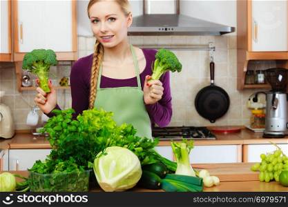 Woman in kitchen with many green leafy vegetables, fresh produce on counter. Young housewife holding broccoli in hand. Healthy eating, cooking, vegetarian food, dieting and people concept.. Woman in kitchen with green vegetables broccoli in hand