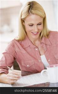 Woman in kitchen with newspaper and coffee smiling