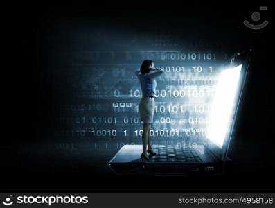 Woman in light of laptop screen. Young businesswoman standing on keyboard of big laptop