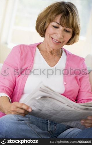 Woman in living room reading newspaper smiling