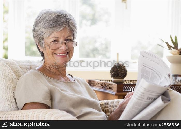 Woman in living room reading newspaper smiling