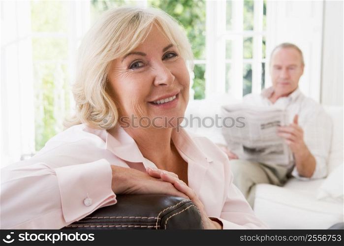 Woman in living room smiling with man in background reading newspaper