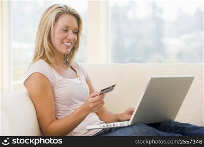 Woman in living room using laptop and holding credit card smiling