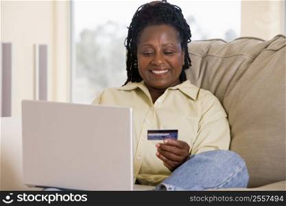 Woman in living room using laptop holding credit card and smiling