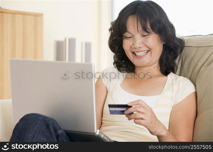 Woman in living room using laptop holding credit card and smiling
