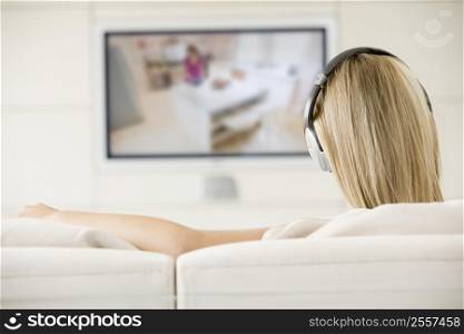Woman in living room watching television and wearing headphones