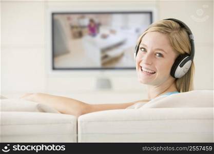Woman in living room watching television and wearing headphones smiling