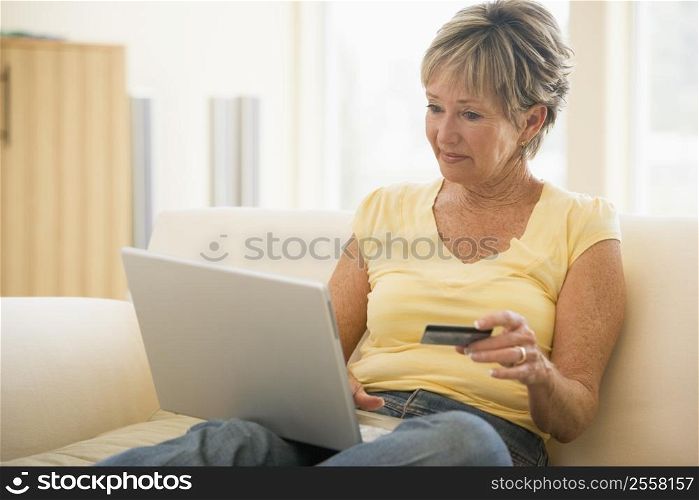 Woman in living room with laptop and credit card smiling