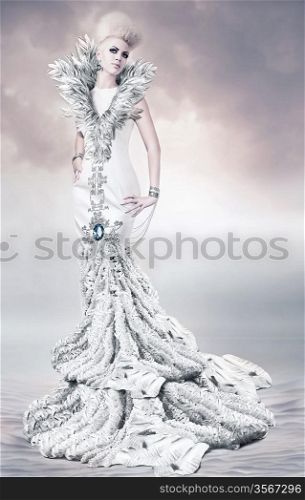 woman in long white dress with feather collar on sand