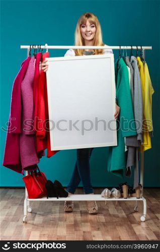 Woman in mall wardrobe with blank banner copyspace. Happy smiling pretty woman in wardrobe holding blank empty banner. Gorgeous girl customer in mall shop with copyspace. Fashion clothing sale advertisement concept.
