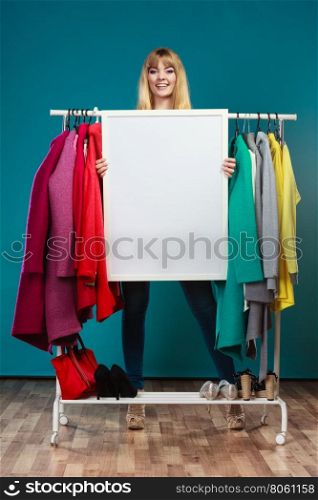 Woman in mall wardrobe with blank banner copyspace. Happy smiling pretty woman in wardrobe holding blank empty banner. Gorgeous girl customer in mall shop with copyspace. Fashion clothing sale advertisement concept.