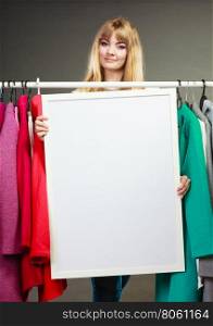 Woman in mall wardrobe with blank banner copyspace. Pretty woman in wardrobe holding blank empty banner. Gorgeous girl customer in mall shop with copyspace. Fashion clothing sale advertisement concept.