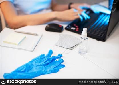 Woman in mask, working from home. Sanitizer anti virus spray on the working table. Coronavirus, quarantine for COVID-19 concept.. Woman in quarantine for coronavirus working from home
