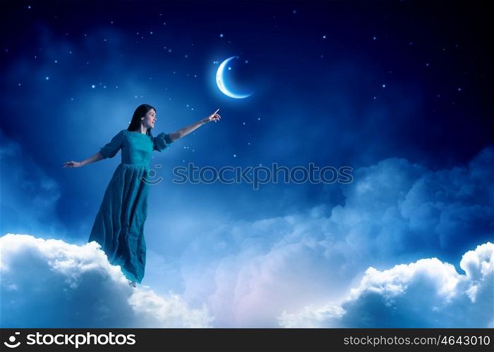 Woman in night sky. Elegant woman in green long dress walking on clouds