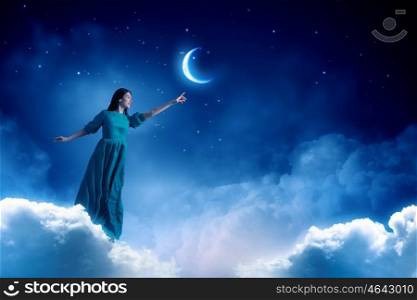 Woman in night sky. Elegant woman in green long dress walking on clouds