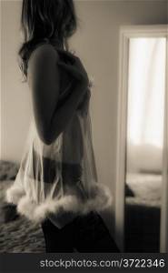 Woman in nightdress posing front of mirror, tinted black and white image, vertical format