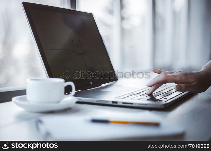 Woman in office using laptop and notepad to work. Shallow depth of field.