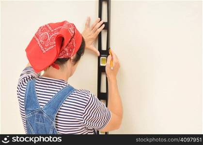 Woman in overalls marking straight line on wall