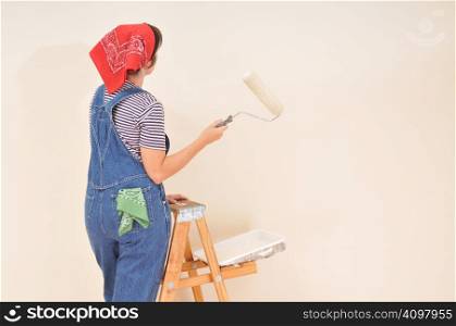 Woman in overalls standing on ladder with paint roller