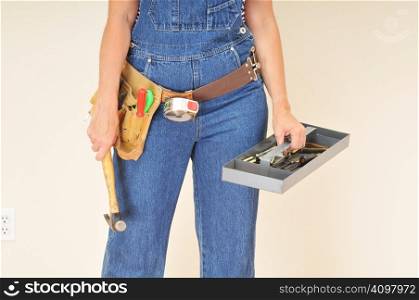 Woman in overalls wearing a tool belt and carrying a tool tray