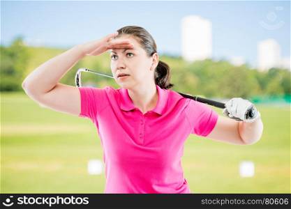woman in pink T-shirt with a golf club looks into the distance on a background of golf courses