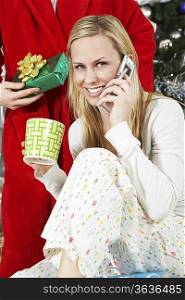 Woman in pyjamas on cell phone in front of man holding Christmas present