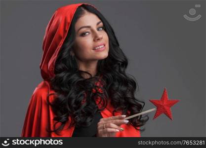 Woman in red cape with star shaped magic wand , gray background. Woman in red cape with magic wand