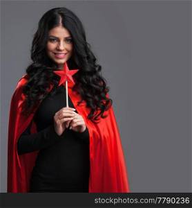 Woman in red cape with star shaped magic wand, gray background. Woman with star shaped magic wand