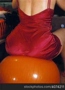 Woman in red negligee sitting on an orange exercise ball
