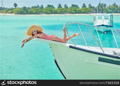 Woman in red striped one-piece swimsuit lying on boat bow. Summer vacation at Maldives.