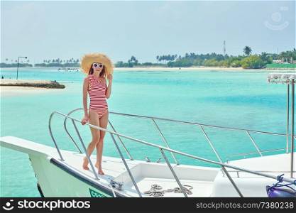 Woman in red striped one-piece swimsuit standing on boat bow. Summer vacation at Maldives.
